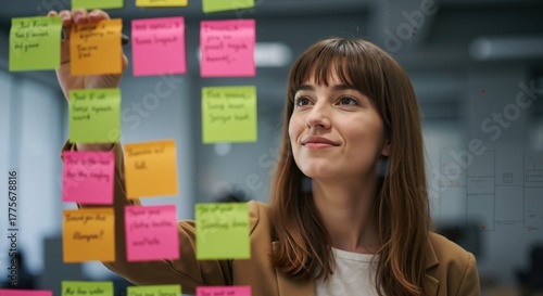Creative professional woman brainstorming ideas with colorful sticky notes on glass board. Businesswoman working on project management and strategic planning in modern office