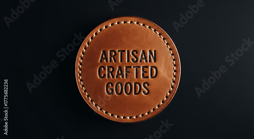 Close up of an oval shaped leather tag with embossed text reading artisan crafted goods and detailed stitching against a dark background