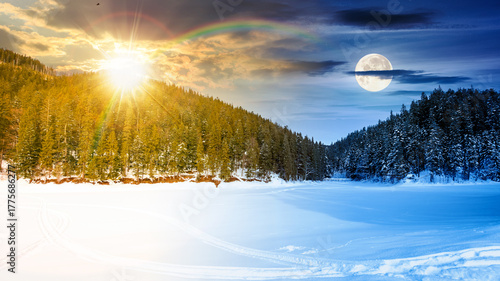 winter landscape with snow covered ground. day and night time change concept. frozen lake among spruce forest with sun and moon. panoramic view of winter wonderland. duality and transition template