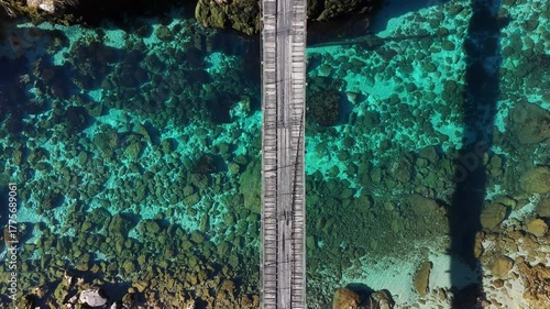 Drone shot over a wooden bridge crossing the vivid blue Piva River Canyon in Montenegro.