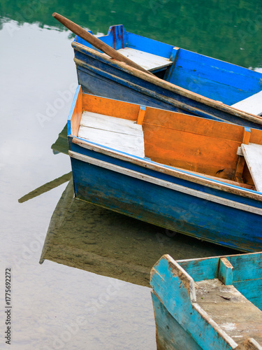 Colorful wooden boats reflecting in calm water at a serene lakeside location during daylight hours