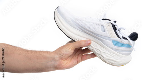 Hand holding a white sports shoe against a plain background in a bright setting