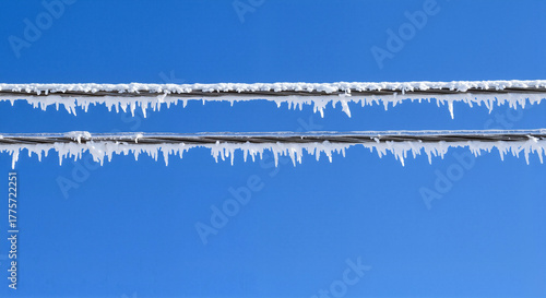 Icicles hanging from power lines against a clear blue winter sky  