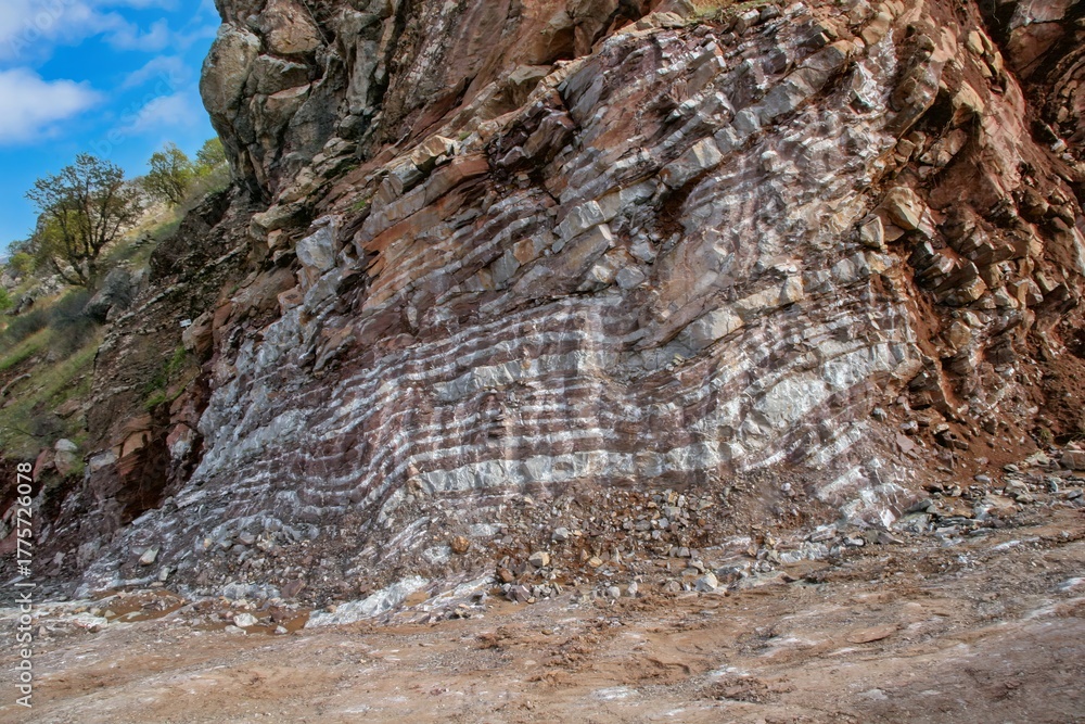 Naklejka premium Layered rock formations of the Zagros Mountains, featuring distinctive red and green sedimentary strata under a clear sky in Kurdistan