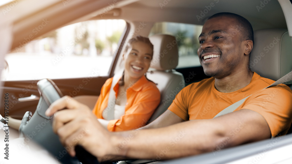Fototapeta premium Happy young black couple enjoying relaxed moment while driving car together, african american spouses laughing and sharing fun conversation inside automobile
