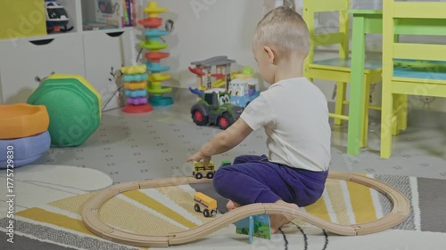 Toddler boy playing with wooden train set in playroom
