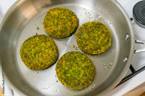 Top view of four veggie burger patties frying in stainless steel pan, natural and vegetarian food concept