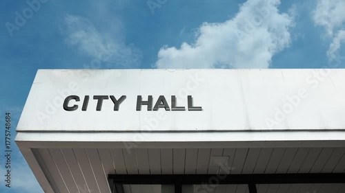 City Hall word sign prominently displayed on the official, civic facade of a grand government building beneath a clear blue sky, signifying the central municipal administration and public offices