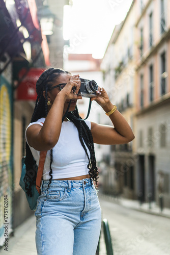 Smiling Latina woman with braided hair using an analog camera on the street