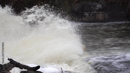 A powerful, rapid river current vigorously encounters an obstacle, creating an impressive and dramatic burst of foaming slush. The raw energy of flowing water in nature.
