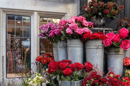 Fotografia A vibrant outdoor display of fresh flowers for sale, featuring bouquets of deep red and bright pink roses arranged in rustic galvanized metal buckets
