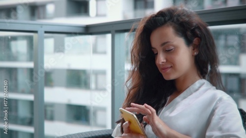 Photography Beautiful young woman sitting on a balcony and texting on smartphone browsing on social media