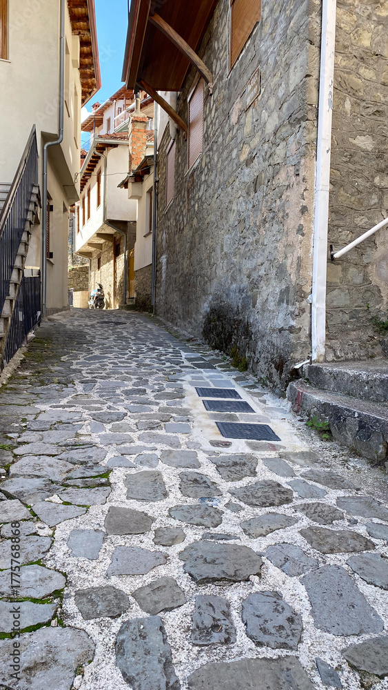 Obraz premium Charming narrow cobblestone alleyway with rustic stone buildings and blue sky