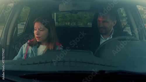 Caucasian teenager sitting in vehicle in front seat. Cheerful Caucasian handsome man waiting in car on little girl. Close up. Dad picks up daughter in car. Family concept. Slow motion