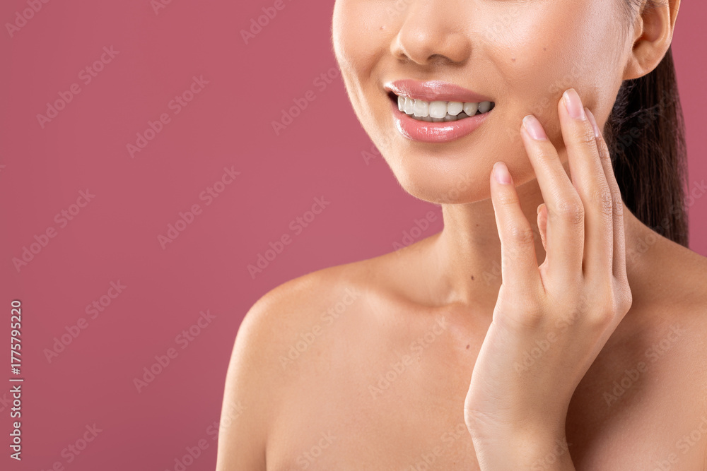 Fototapeta premium Unrecognizable young lady touches her face while showing off a perfect white smile against a purple background. This cropped shot highlights the importance of dental care and oral hygiene.