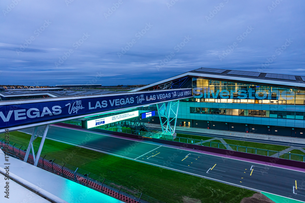 Obraz premium The Silverstone pit building lit up at twilight, ideal for motorsport, travel, and architecture themes.