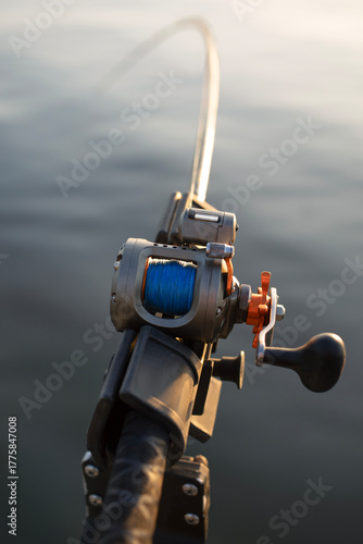 A close-up photo of a fishing rod and reel during a summer fishing trip. The background shows calm, out-of-focus water.