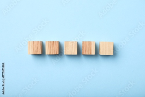 Wooden cubes on light blue background, top view