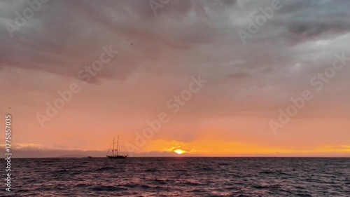 A magnificent sunset while sailing on the Aegean Sea. A sailboat sails in the distance.
