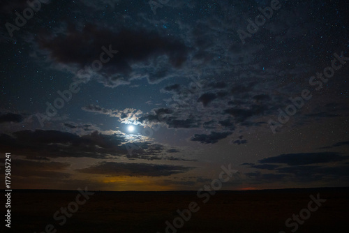 The moon and stars shining through clouds over a prairie