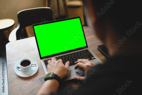 A man's hands typing on a laptop with a blank green screen in a cafe. Ideal for chroma key compositing to add custom video or website content.