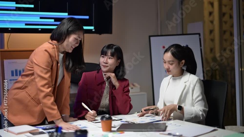 Three women are sitting at a table, smiling and talking to each other. They are dressed in business attire and appear to be having a friendly conversation
