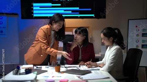 Three women are sitting at a table with a large monitor behind them. They are smiling and seem to be having a good time