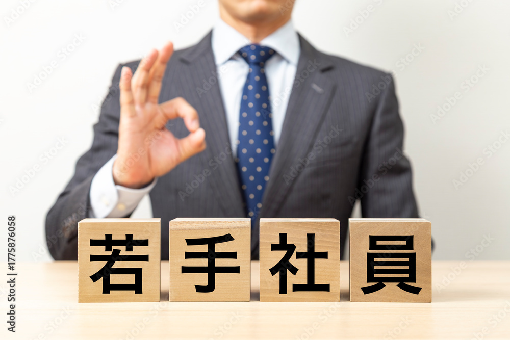 Obraz premium 「若手社員」と書かれたブロックとOKポーズをするビジネスマン