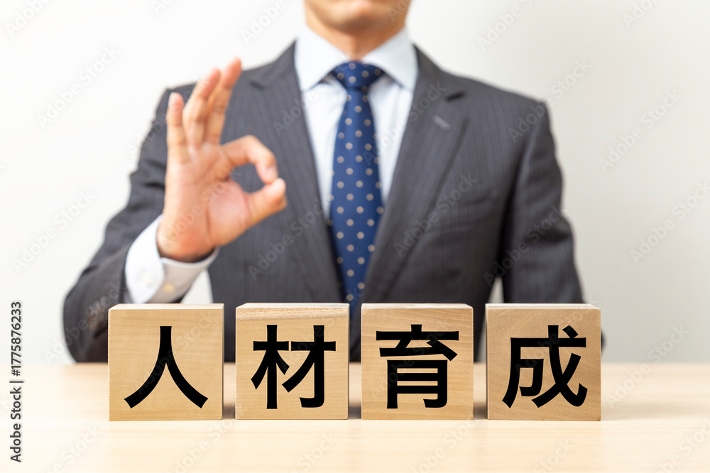 Obraz premium 「人材育成」と書かれたブロックとOKポーズをするビジネスマン