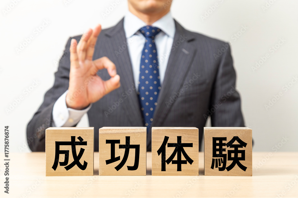 Obraz premium 「成功体験」と書かれたブロックとOKポーズをするビジネスマン