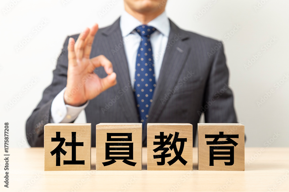Obraz premium 「社員教育」と書かれたブロックとOKポーズをするビジネスマン