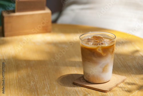 a glass of iced milk coffee on wooden table in sun light and shade