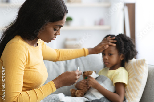 Photos Mother is attentively checking the temperature of her child while sitting on a couch