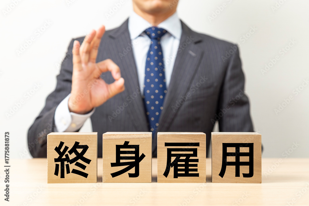 Obraz premium 「終身雇用」と書かれたブロックとOKポーズをするビジネスマン