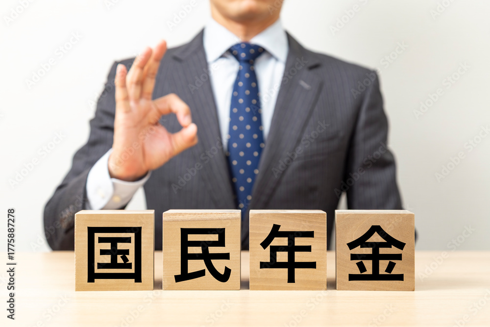 Obraz premium 「国民年金」と書かれたブロックとOKポーズをするビジネスマン