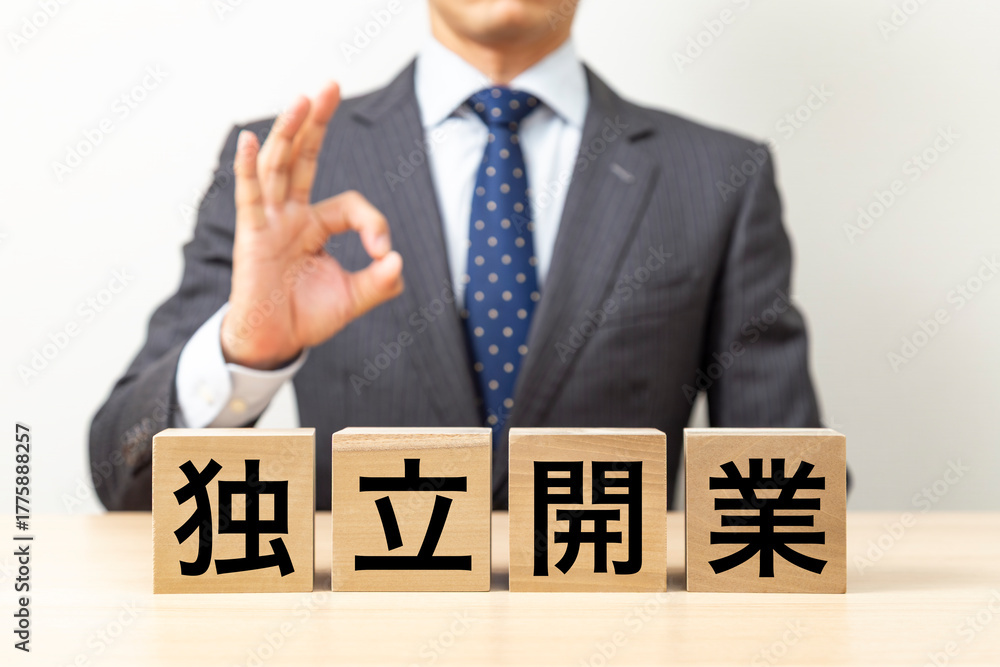Obraz premium 「独立開業」と書かれたブロックとOKポーズをするビジネスマン