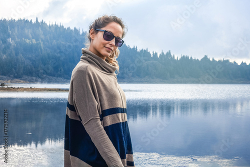 Young Woman Wearing Cozy Sweater Outdoors by a Peaceful Lake