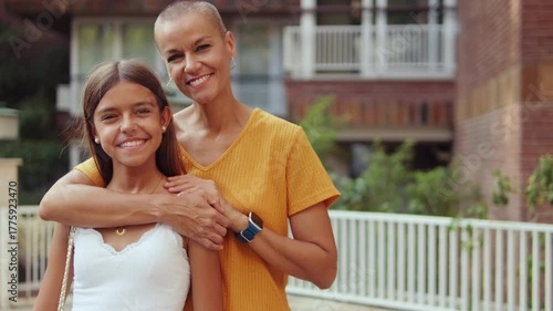 Mother and Daughter walk down the street with their arms around each other, enjoying each other's company on a sunny day.