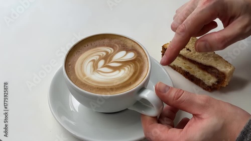 white ceramic cup filled with frothy coffee alongside a sliced portion of baked dessert on a plain white