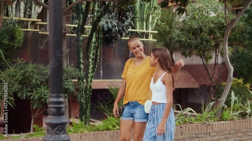 A mother with short hair and her daughter walk hand in hand, chatting and laughing. They enjoy a stroll on a sunny day.