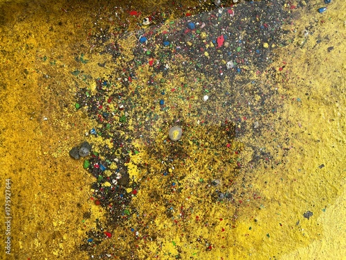 Yellow wall texture with dark wet spots and multicolor paint splashes forming unique abstract pattern.