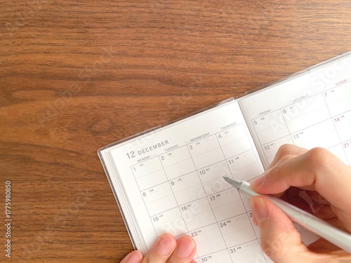 Tableau sur toile Woman's hand filling out a December schedule book on a wooden table