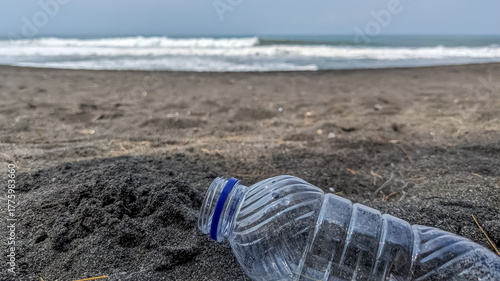 Plastic bottle washed up on black sand beach near crashing waves highlights ocean pollution crisis, environmental concerns, sustainability, and coastal issues