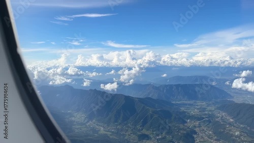 View from an airplane window, showing a landscape of mountains, clouds, and sky