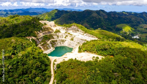 Aerial view of open-pit mine/quarry, bright blue water, surrounded by lush green hills and tropical forest