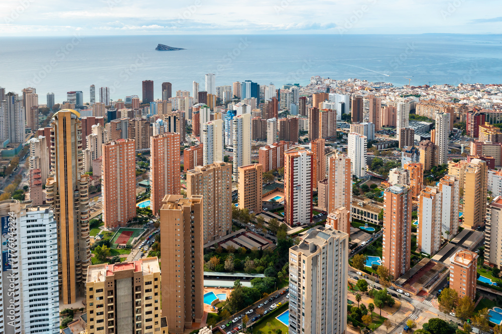 Naklejka premium Panoramic city view of Benidorm modern skyline with high-rise hotels, beachside resorts, and the sparkling Mediterranean Sea. Popular tourist destination in the Alicante region of Spain.