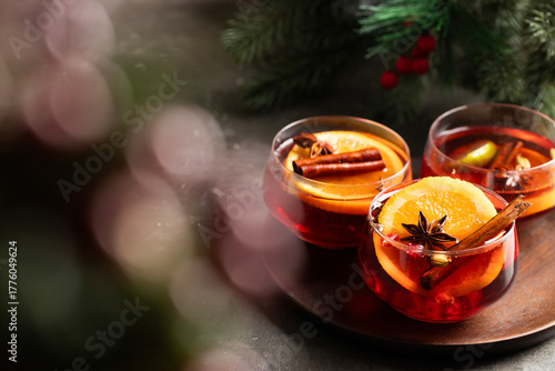 Fototapeta Naklejka Na Ścianę i Meble -  Festive drink with red wine, cinnamon, and orange, styled with seasonal greenery. A delicious symbol of Christmas cheer and cozy holiday evenings.