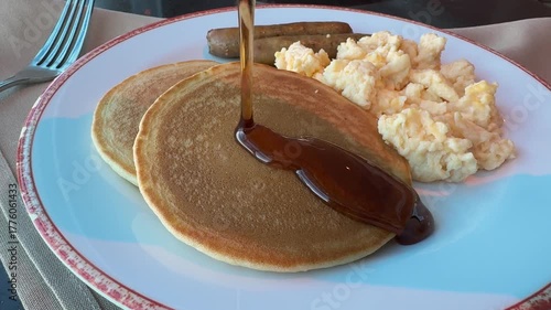 Closeup of Pouring Syrup on Pancakes with Scrambled Eggs and Sausages