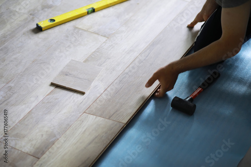 Installing laminated floor, detail on man hands blue wooden tile, over white foam base layer, small pile with more tiles background