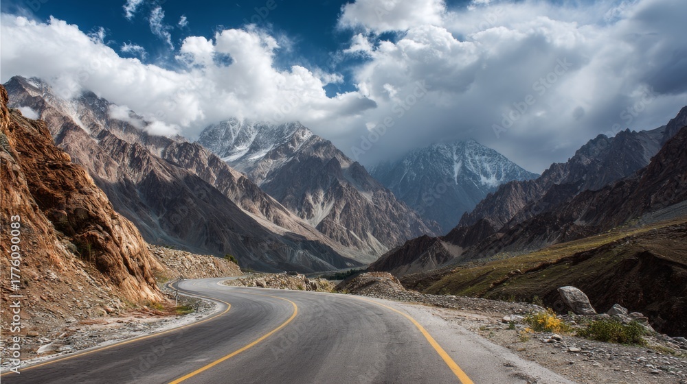 Fototapeta premium Majestic Mountain Landscape with Winding Road Surrounded by Dramatic Peaks and Cloudy Sky in Scenic Natural Environment